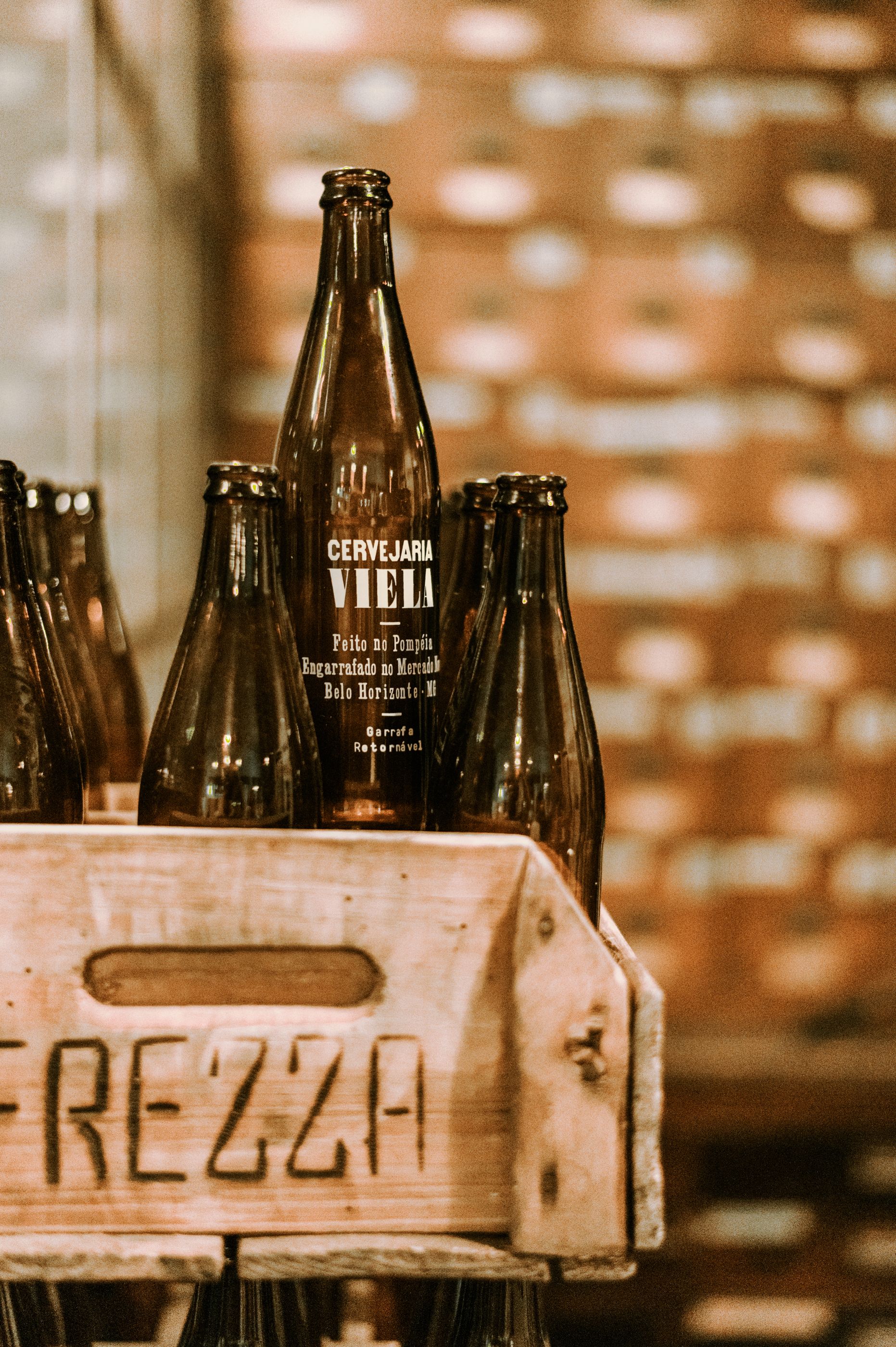 Dark glass bottles clustered in a wooden crate under moody amber light — the tasting case, lit as if just arrived at the market booth.
